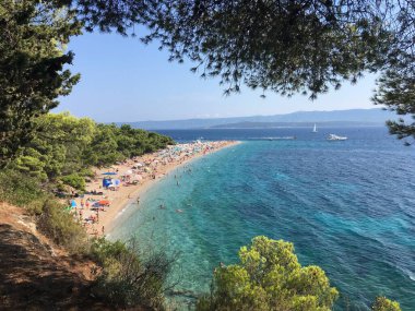 Zlatni Rats 'in ikonik çakıl taşı sütyen üzerine çam ağaçları ve Bols Akdeniz mimarisi tarafından desteklenen hava görüntüleriyle yansıtılıyor..