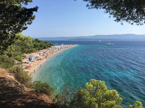 Zlatni Rats 'in ikonik çakıl taşı sütyen üzerine çam ağaçları ve Bols Akdeniz mimarisi tarafından desteklenen hava görüntüleriyle yansıtılıyor..