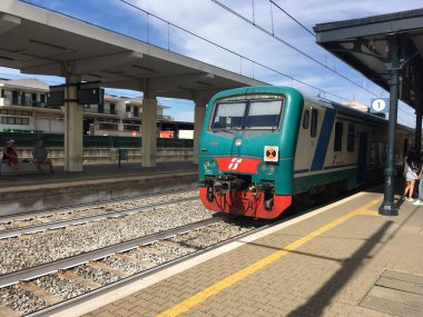 İtalyan yolcu treni istasyon platformunda bölgesel vagonları, beton yüzeyleri, tabelaları ve gün ışığı altında tipik platform detaylarıyla