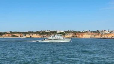 Donanma gemisi Portimo yakınlarındaki Arade Nehri boyunca ilerliyor. Askeri gemileri, nehri, denizi, kentsel binaları ve sokak manzaralarını gösteriyor.