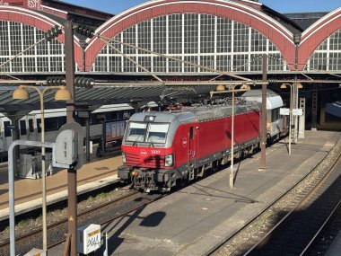 Danish State Railways DSB train positioned on tracks at Copenhagen Central Station platform with overhead lines and station architecture visible in background.