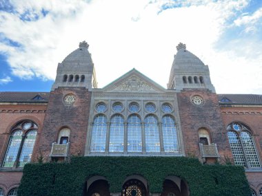 Exterior view of Copenhagen City Hall in Denmark built 1905 by Martin Nyrop showing richly decorated front with Italian-inspired elements gilded statue of founder Absalon above balcony and prominent slim clock tower amid urban square setting.