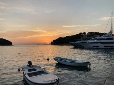Cavtat limanında demirlemiş teknelerle gün batımı sahnesi, Hırvat Adriyatik kıyıları boyunca sakin suları gösteriyor.