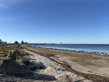 Bright sunlight on Landskrona Sweden coastal area featuring Oresund strait horizon sandy beach and gentle waves with clear weather conditions.