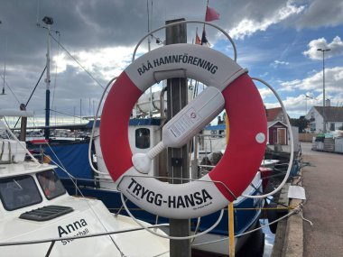 Red-mounted emergency lifebuoy rings located along waterways in Sweden and Denmark, showing white ring buoys with reflective strips and coiled ropes for immediate deployment in drowning incidents near harbors and lakes.