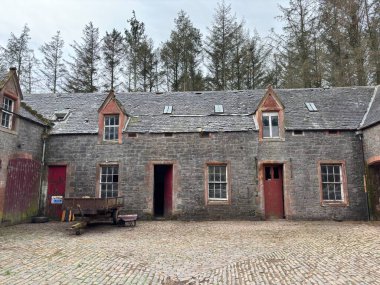 Dilapidated horse stables associated with Thirlestane Castle near Lauder in Scottish Borders, displaying partial stone walls with pointed arches, collapsed roof sections, timber remnants, surrounding grassland, mature trees