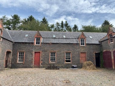 Dilapidated horse stables associated with Thirlestane Castle near Lauder in Scottish Borders, displaying partial stone walls with pointed arches, collapsed roof sections, timber remnants, surrounding grassland, mature trees