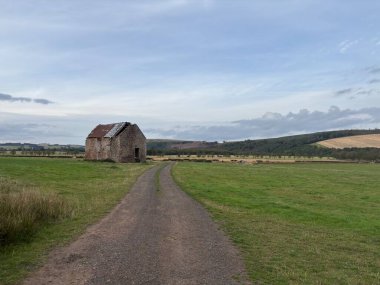 Remains of late 18th century Norton Farmhouse near Lauder in Scottish Borders, displaying unoccupied 2-storey rectangular building with gabled ends, weathered stone facade, timber remnants, and adjacent grassy fields under open sky.