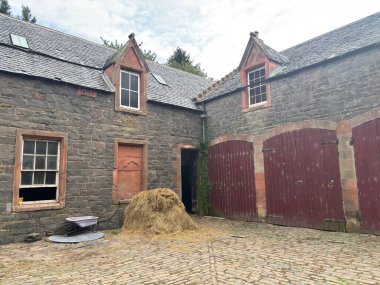 Dilapidated horse stables associated with Thirlestane Castle near Lauder in Scottish Borders, displaying partial stone walls with pointed arches, collapsed roof sections, timber remnants, surrounding grassland, mature trees
