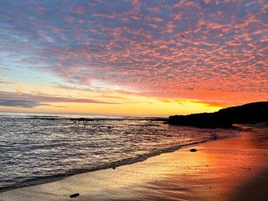 Kumsal boyunca gün batımı kumdaki renkleri yansıtır.