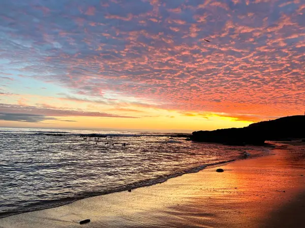 Kumsal boyunca gün batımı kumdaki renkleri yansıtır.