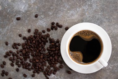 Kahve çekirdekli eski bir çimento masasının üzerine beyaz bardakta sade kahve..