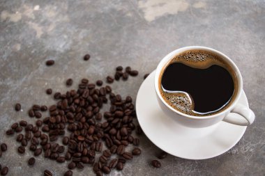 Kahve çekirdekli eski bir çimento masasının üzerine beyaz bardakta sade kahve..