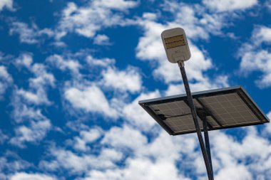 Gökyüzünde güneş enerjisiyle çalışan bir sokak lambası yanıyor. Işık parlıyor ve gökyüzü açık.