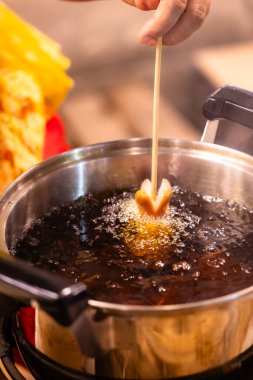 Bir insan tavada sosisli pişiriyor. Tava yağ ile dolu ve sosisliler içine batırılıyor.