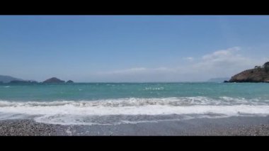 Turkuaz su bir çakıl taşlı plajı, yaz günü, arka planda kayalar ve dağlar, kıyıya vuran deniz köpüğü, Türk plajları, turistik tatil, deniz havası
