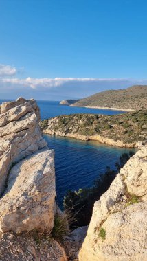 Güneşli bir gün, deniz körfezi, mavi gök mavisi su, bükülmüş kayalar, dik uçurum, güneş ışınları tüm boşluğu dolduruyor.