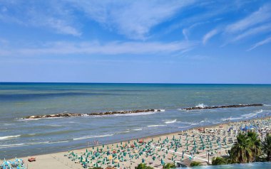 Spiaggia con gli ombrelloni ad agosto ed una scogliera