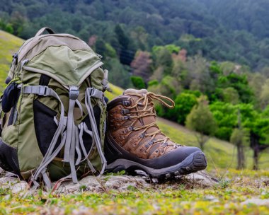 Bir çift yıpranmış yürüyüş botu, dağlık arazide toprak ve tozla kaplı, ve bir seyahat çantası. Konsept, macera yolculuğu.