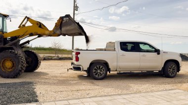 A forklift unloads crushed stone into a vehicle. High quality photo clipart