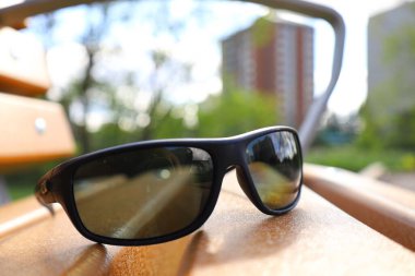 Tahta bir yüzeyde duran siyah güneş gözlükleri şehir binalarını ve gökyüzünü yansıtıyor..