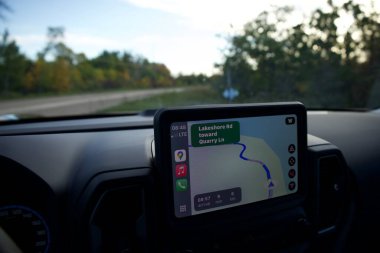 Bir rota gösteren bir araba navigasyon sistemi. Kontrol düğmeleri ve gösterge paneli olan direksiyon arka planda yol olan görünür..