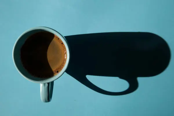 Mavi arka planda mavi kahve fincanı, uzun bir gölge.