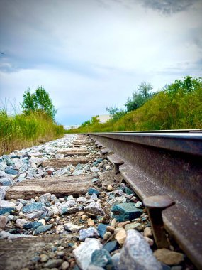 railway track with rocks and grass under a cloudy sky clipart