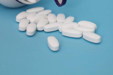 Beyaz tabletler dağılmış ve mavi arka planda mavi kapsülleri olan su toplamış.