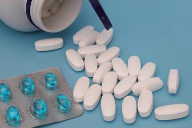 Beyaz tabletler dağılmış ve mavi arka planda mavi kapsülleri olan su toplamış.