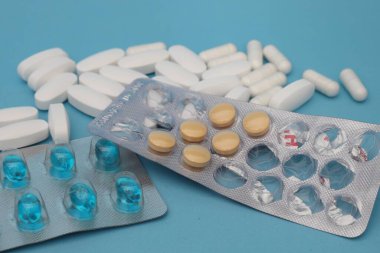 Beyaz tabletler dağılmış ve mavi arka planda mavi kapsülleri olan su toplamış.