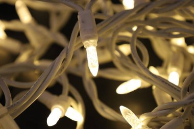 Karmaşık bir çelenk, parlak ampuller ve siyah arka planda beyaz kablolar.