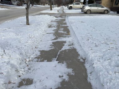 a winter sidewalk cleared of snow, with snowbanks on the sides. in the background, cars and trees line the road. clipart