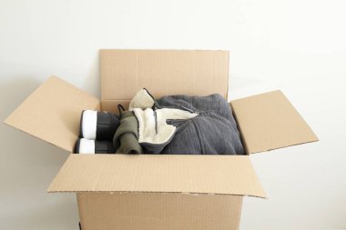 Elbiselerle dolu açık bir karton kutu, içinde yün kaplamalı bir ceket de var..