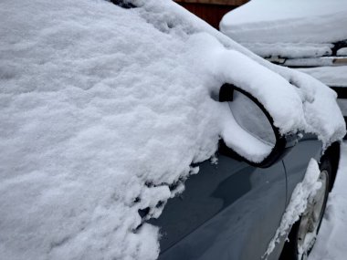 Yoğun karla kaplı bir arabanın yakın plan görüntüsü. Yan aynaya odaklanmış. Kış kar yağışı tabakasının altında kısmen gömülü..