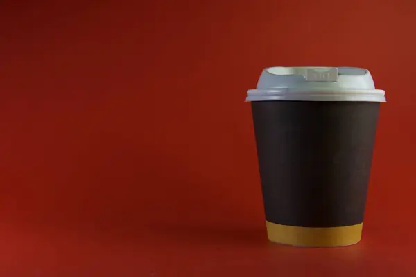 Beyaz plastik kapaklı ve sarı aksanlı siyah bir kahve fincanı, kırmızı arka planda..