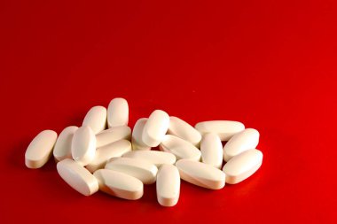 Beyaz magnezyum B6 oval şekilli tabletler parlak kırmızı bir zemin üzerinde uzanıp tıbbi amaçlarını vurguluyorlar.