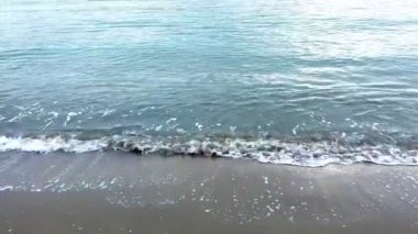 Kumlu bir sahilde sörf, kumlu bir sahilde küçük dalgalar, sakin bir atmosfer.