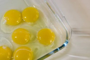 Açık renkli bir yüzeye yerleştirilmiş yumurta beyazlarıyla çevrili cam bir kapta altı çiğ yumurta sarısı..