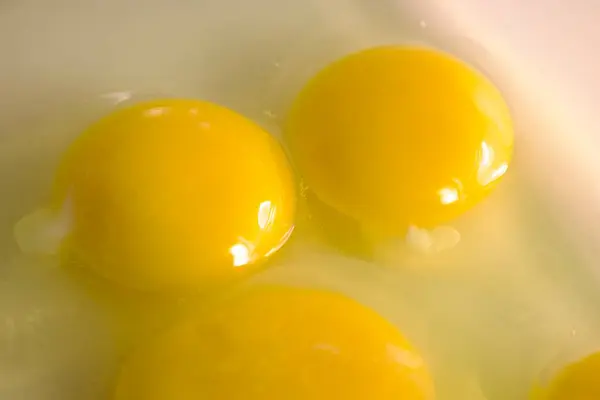 Açık renkli bir yüzeye yerleştirilmiş yumurta beyazlarıyla çevrili cam bir kapta altı çiğ yumurta sarısı..