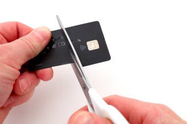 Siyah bir plastik kartı makasla kesmek, ellerin ve kartın yakın görüntüsü..