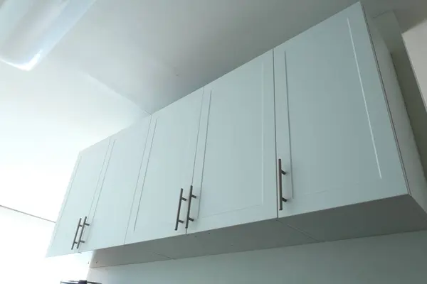 Beyaz mutfak dolapları, buzdolabının üstünde mikrodalga fırın, minimalist iç mekan, temiz ve basit tasarım..