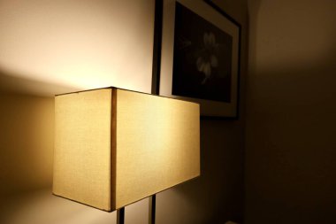 Dikdörtgen bir abajurdan gelen sıcak ışık, yakınındaki siyah-beyaz bir resimle duvarı aydınlatıyor.