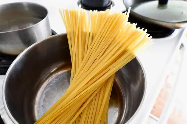 Yanında pişirilmemiş spagetti ile kaynatılmaya hazır bir tencere ve diğer mutfak aletleri var.
