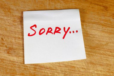 Tahta bir yüzey üzerinde beyaz bir kağıt parçası uzanıyor. Üzerinde el yazısı yazılı. Üzgünüm, kırmızı mürekkeple..