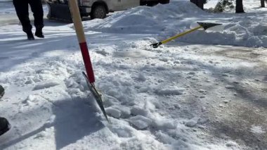 Bir adam kaldırımdan metal bir kazıyıcıyla buz temizliyor.