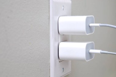 two white chargers plugged into a wall outlet, gray background, connected cables for device charging. clipart