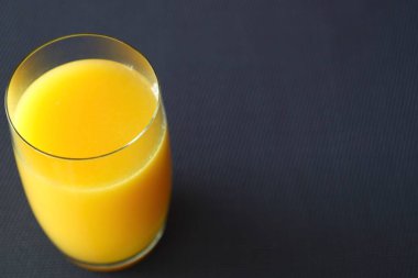 Mavi bir masa örtüsüne yerleştirilmiş, içi taze sarı-portakal suyuyla dolu şeffaf bir bardağın yakın çekimi..
