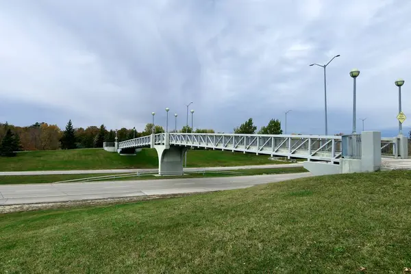 Yol üzerindeki yaya köprüsü, yeşil çimen, sonbahar ağaçları, sokak lambaları, bulutlu gökyüzü, şehir manzarası