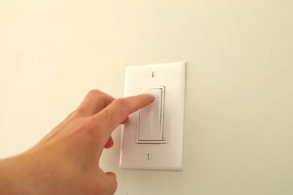 Bir insan iki parmağıyla açık renkli bir duvarda duvar lambası düğmesine basar..